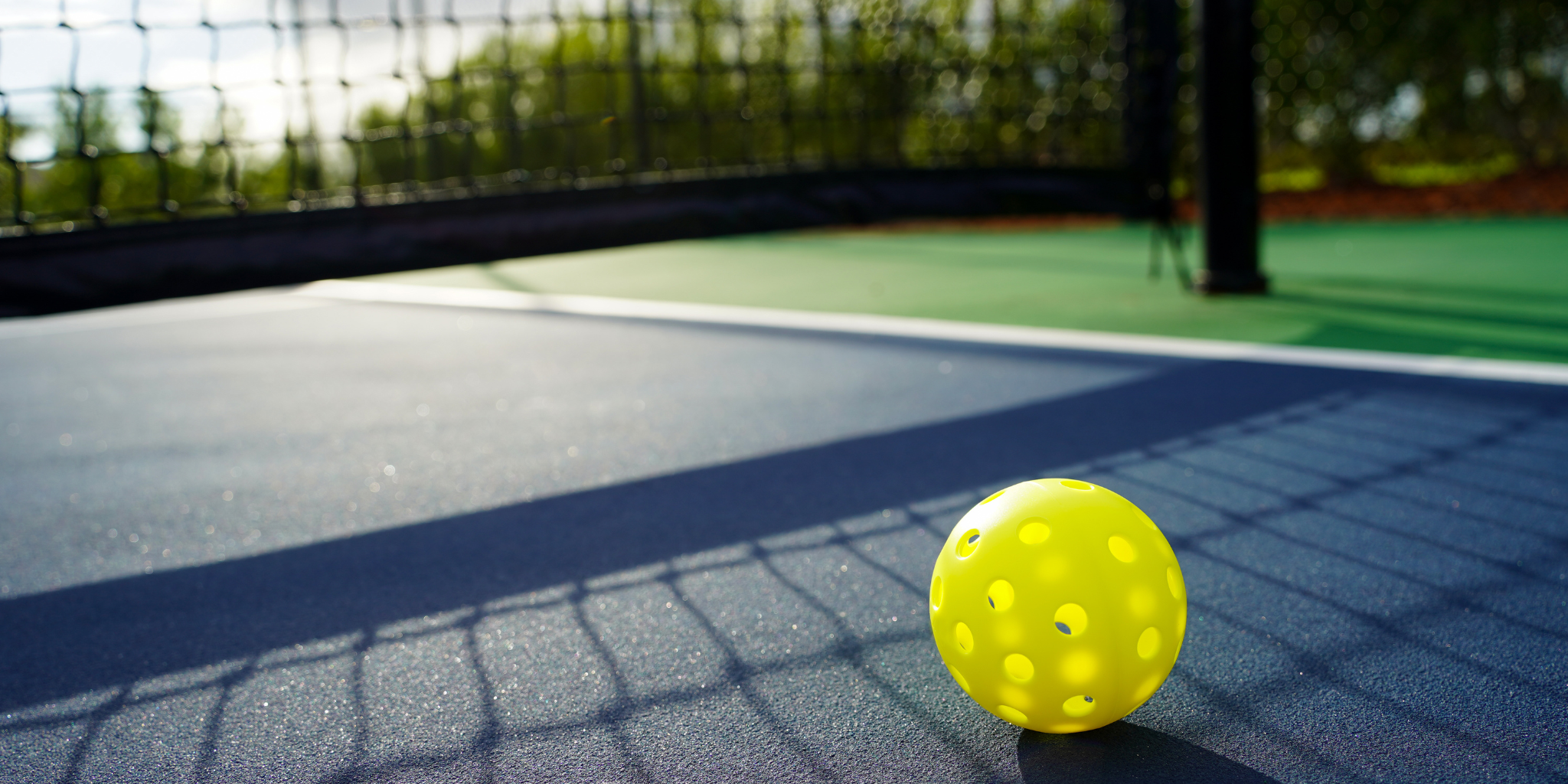 Yellow pickleball on a blue pickleball court with green net and background
